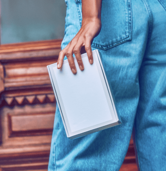 lower half of a women wearing jeans standing in front of a wooden door and holding an iqos box